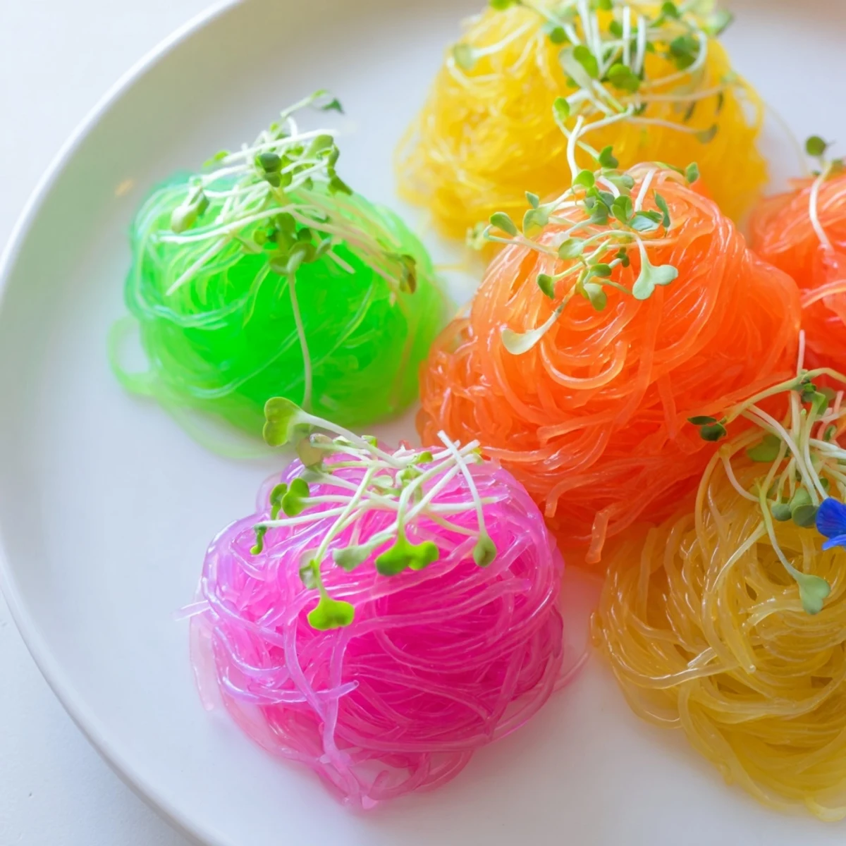 Vibrant neon noodle clouds served chilled with soy dipping sauce, a playful, eye-catching dish.
