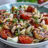 A vibrant summer pasta salad with cherry tomatoes, mozzarella, and fresh basil in a light balsamic dressing.