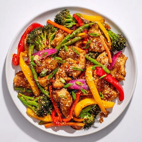Golden-brown sheet pan chicken stir-fry with a sprinkle of sesame seeds and sliced green onions.