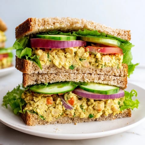 Golden-brown whole grain bread holds a delicious Easy Chickpea Salad Sandwich, ready to eat now.