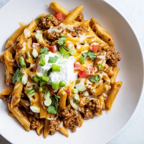 A steaming bowl of One-Pot Taco Pasta with melted cheese and fresh green onion toppings.
