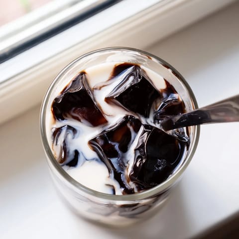 A glass of Coffee Jelly Drink features bouncy coffee cubes in creamy milk, garnished with a straw and ready to enjoy.