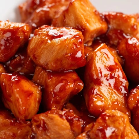 Close-up of a sweet chili chicken bowl showing tender chicken pieces in sticky sauce over rice with fresh green onion garnish.  