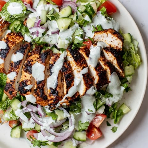 A close-up of vibrant Chicken Shawarma Salad showcasing crisp greens and diced vegetables, topped with golden-brown grilled chicken and a tangy garlic yogurt sauce.