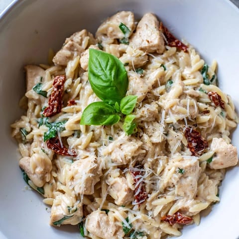 Golden, cheesy Tuscan Chicken Orzo in a deep pan, garnished with fresh basil and a spoon ready to serve.