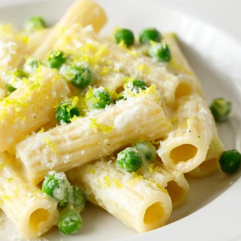 In a rustic kitchen setting, a fork lifts a bite of Pea & Lemon Ricotta Pasta, showing the silky ricotta-lemon sauce and sweet peas against the al dente pasta.