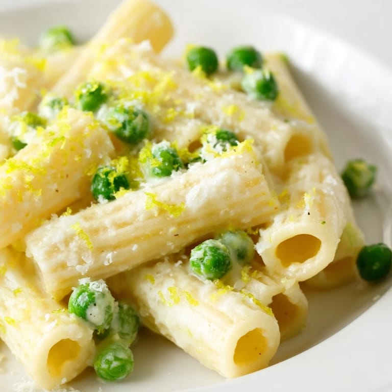 In a rustic kitchen setting, a fork lifts a bite of Pea & Lemon Ricotta Pasta, showing the silky ricotta-lemon sauce and sweet peas against the al dente pasta.