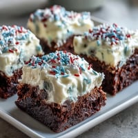 Festive 4th of July Firecracker Brownie Bites topped with creamy vanilla frosting and patriotic red, white, and blue sprinkles.